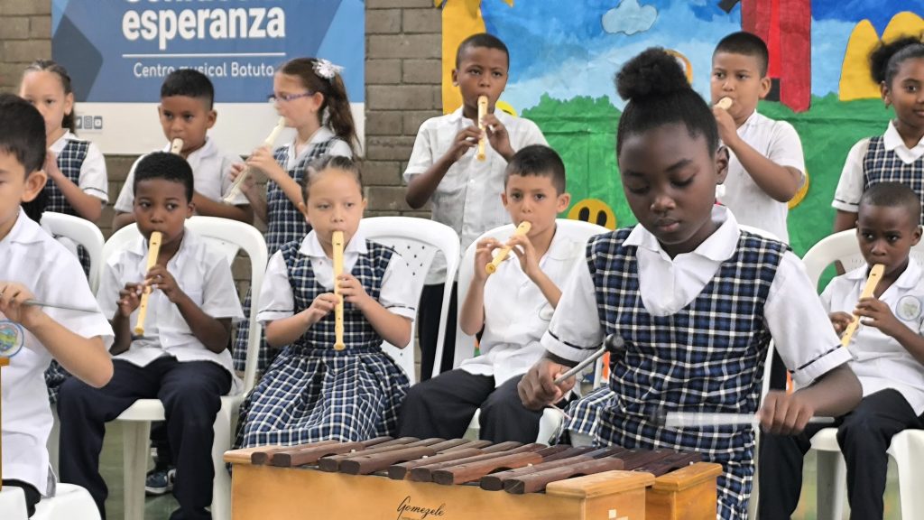 Niña de Cali tocando la marimba en un salón de clases, detrás hay niños y niñas tocando flautas