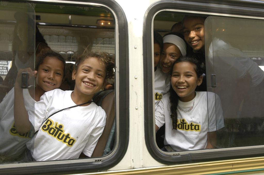 Estudiantes de Batuta del año 2003 asomándose por las ventanas de un autobús sonriendo a la cámara