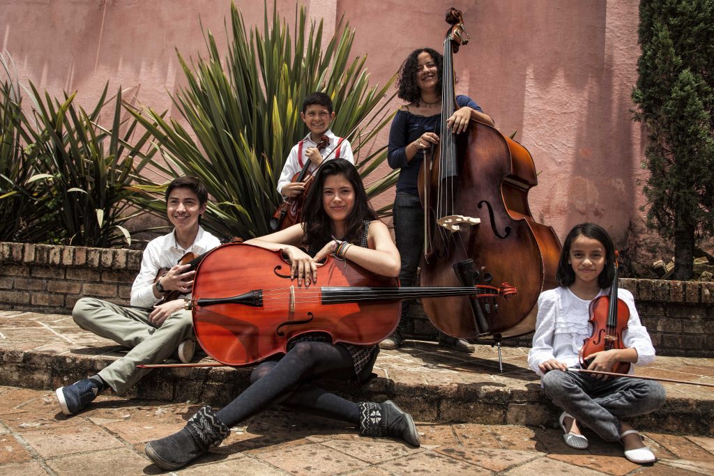 Niños, niñas y jóvenes de la camerata de Buenaventura posan con violines, violonchelos y contrabajos