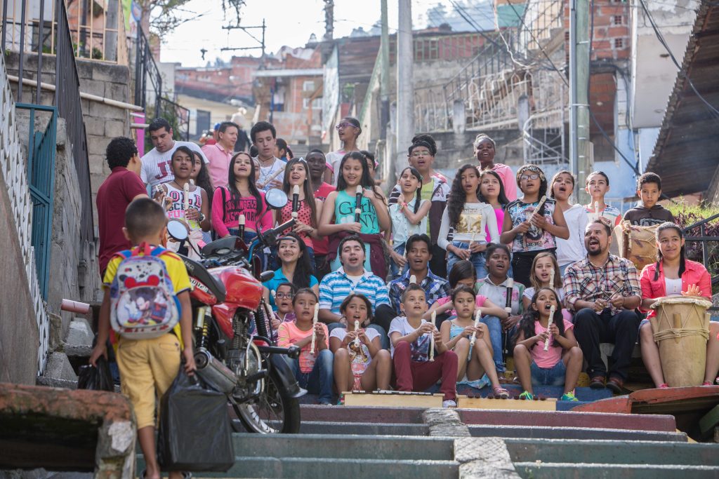 Niños y niñas del Ensamble Estación Madera de la Fundación Batuta sentados en la Comuna 13, sosteniendo flautas dulces, instrumentos de percusión y xilófonos junto a sus profesores.