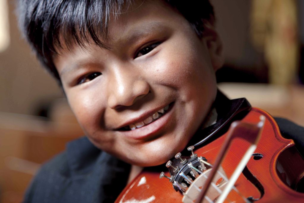 Niño estudiante de la Fundación Nacional Batuta sonríe a la cámara tocando el violín