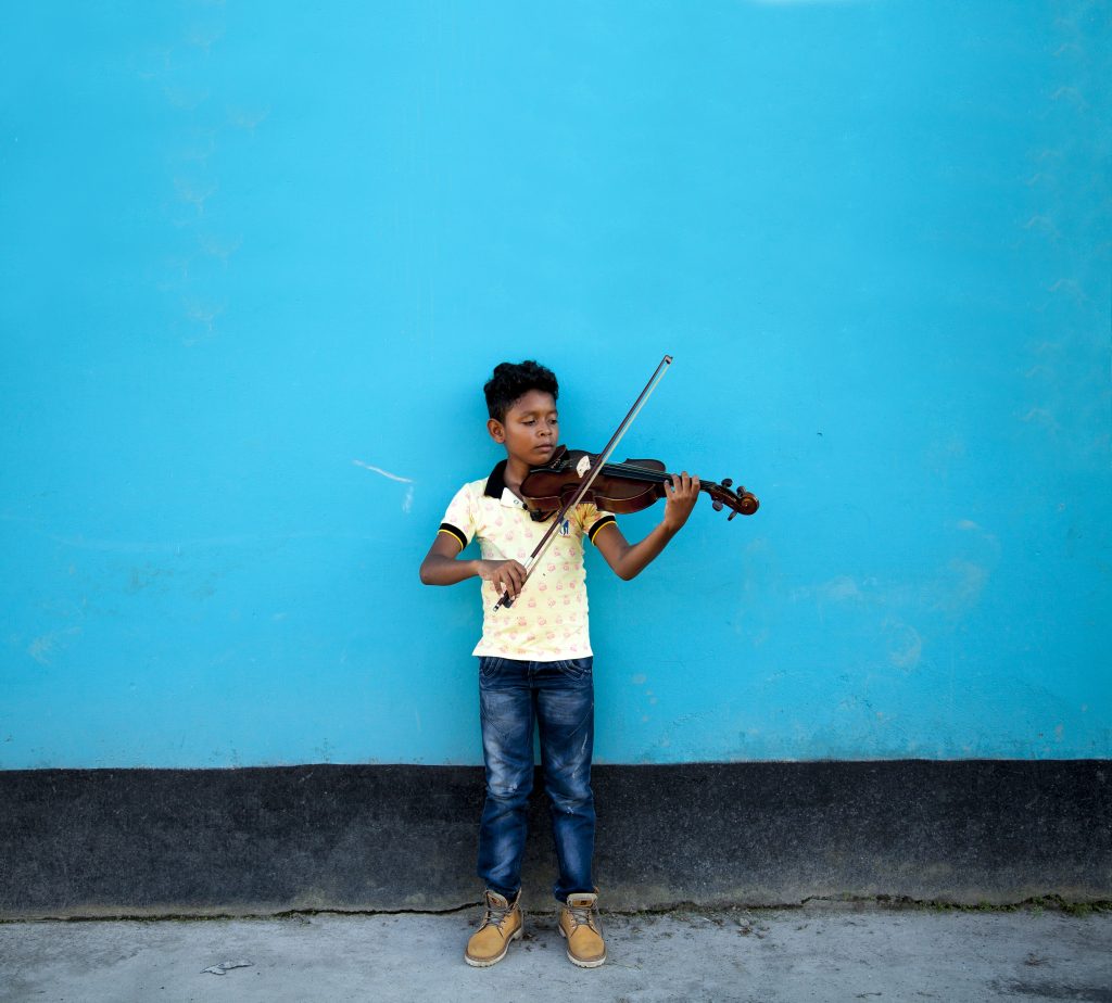 Niño de la Fundación Batuta tocando el violín frente a una pared azul en Puerto Asís.