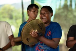 Niño del centro musical Batuta Chocó sonriendo y tocando los platillos musicales