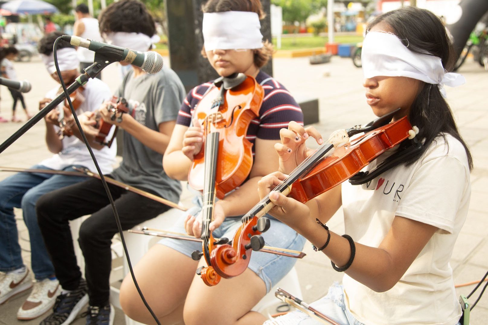 Cuatro niños y niñas sentados con los ojos vendados explorando violines con las manos en un taller