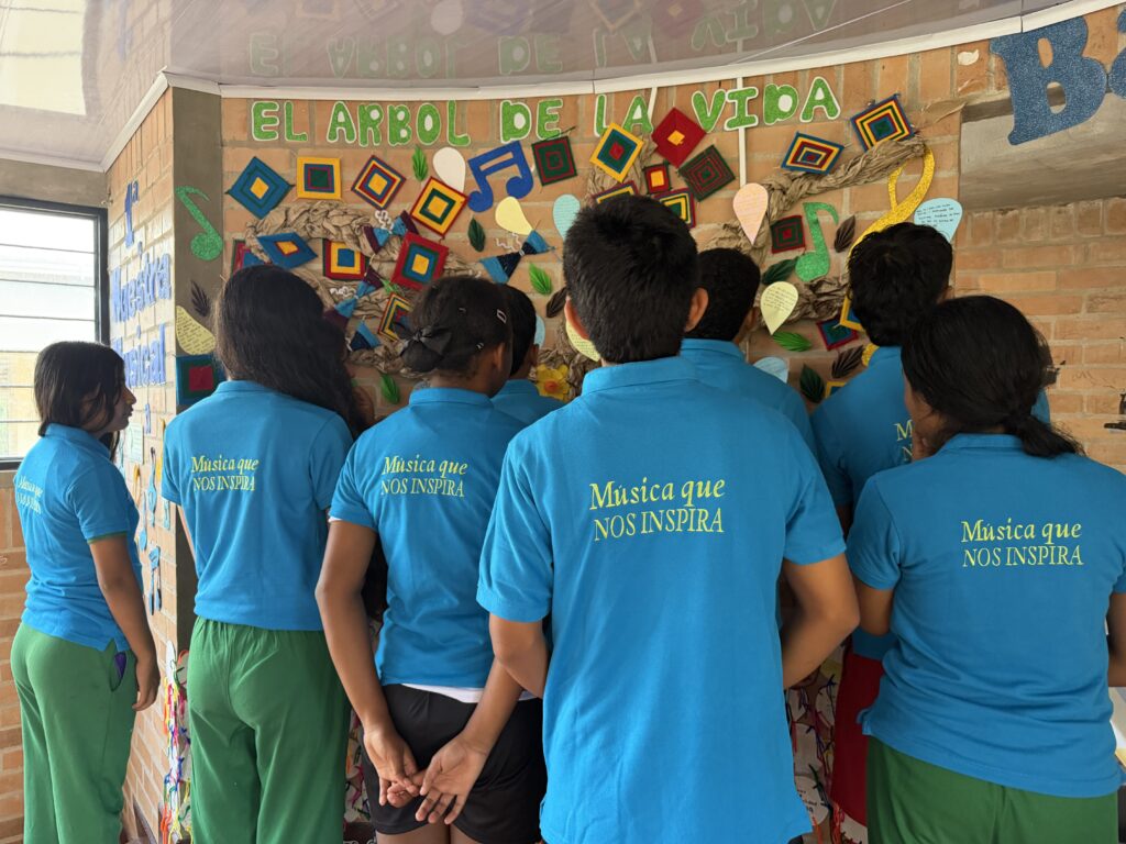 Niños y niñas observando un mural, dando la espalda a la cámara con camisetas con el mensaje "Música que nos inspira"