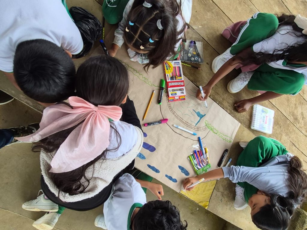 Niñas estudiantes de Batuta sentadas coloreando una cartelera con marcadores durante actividad creativa