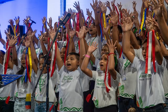 Niños y niñas con banderas de Colombia y Perú en las manos en un concierto