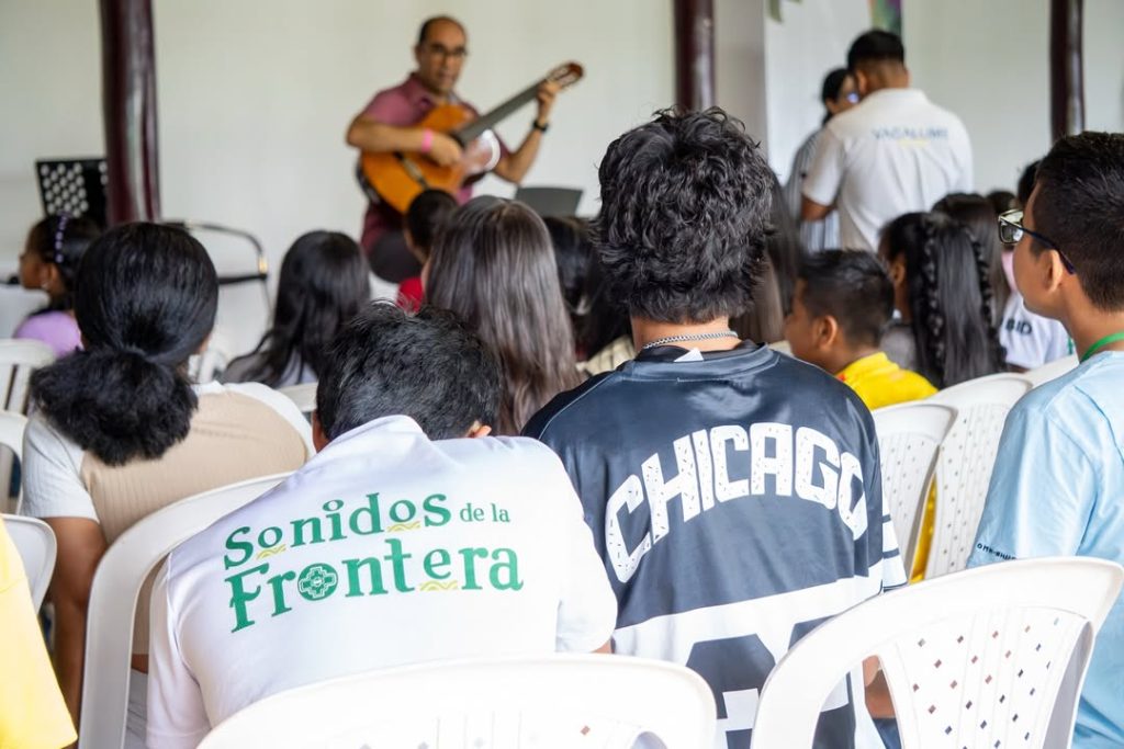 Niños, niñas y jóvenes sentados en clase con el maestro tocando la guitarra