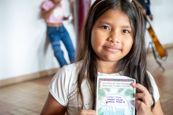 Una niña peruana de Sonidos de la Frontera sonríe a la cámara sosteniendo un dibujo de un manatí