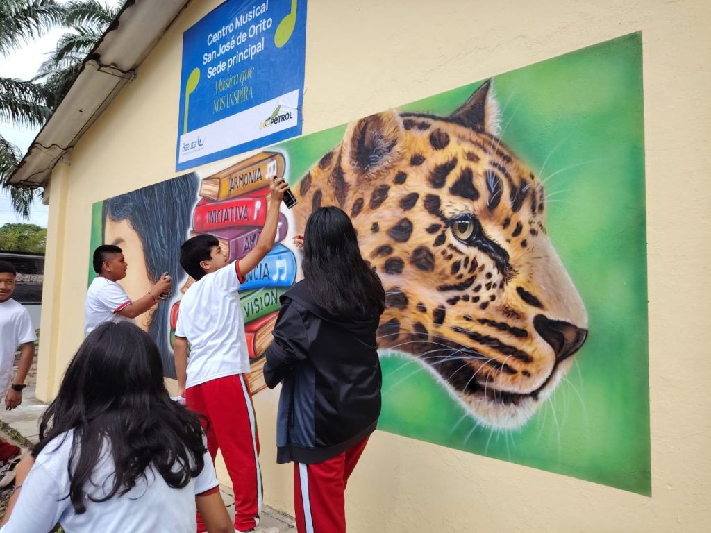 Niños y niñas  del centro musical san josé de orito frente a mural de un jaguar 
